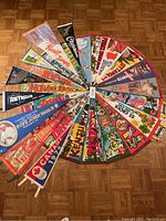 Collection of various vintage pennant flags arranged in a circle on wooden floor, showing multiple colorful designs and some text for locations and events.