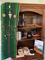 Photo of the full display including a wooden shelf, a green and purple striped textile with many pins attached, books, ceramic vases, and decorative items.