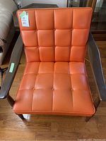 Front view of retro orange vinyl chair showing tufted button design and dark wood armrests and legs.