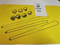 Seven rings and three necklaces laid out on yellow background, showing general condition and design variety