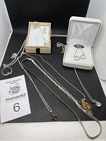 Photo showing multiple silver-colored necklaces, silver ring with gemstone and pendants with amber-like and other stones