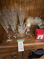 Photo showing 6 crystal-pattern tall glasses, small glass pitcher, metal napkin holders including duck-shaped and ring designs, and condiment set with spoons on tray
