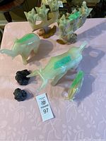 Seven stone animal figurines and candleholders displayed on table with a pink tablecloth. Light green jade-like bull with chip on horn, four birds on stands, and two small black rose candleholders visible.