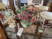 Display cabinet showing three decorative items: a cardinal bird metal plate, porcelain flower arrangement, and glass pedestal bowl