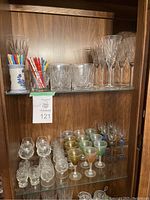 Wide view of glassware assortment in wooden cabinet including tumblers, stemmed glasses, cocktail stick holders with sticks