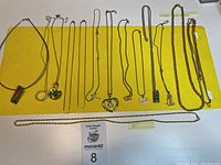 Full display of 14 assorted necklaces laid out on yellow cloth background, showing variety of chain styles and pendants.