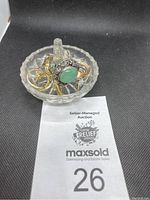 Photo showing several rings stacked on the glass ring holder with a close-up view of the green stone ring and gold and silver rings.