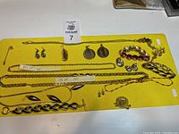 Top view of entire lot showing two gold-tone chain necklaces labeled 14k GP 20" and 22", brooches, pendants, multiple pairs of earrings, bracelets including enamel link bracelet and red string bracelet, and a stick pin.