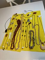 Full overview of the assorted vintage jewelry pieces laid out on a yellow cloth, showing variety in size, style and materials, including pendants, chains and brooches.