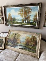 Two of the vintage paintings, showing tree and river landscapes, framed in traditional wood frames in gold and cream color.