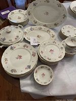 Photo of the 61-piece dinnerware set laid out on table, showing plates, serving dishes, gravy boat, bowls, and saucers, all featuring floral pattern with some chips visible on gravy boat and other pieces.
