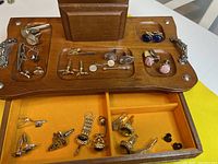 Overhead view of wooden box open showing cufflinks and tie clips in compartments