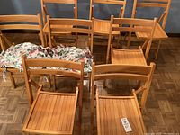 Eight wooden folding chairs arranged in rows with two floral chair pads placed on two chairs.