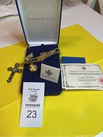 Full view of Camrose & Kross jewelry set in original box showing gold-tone cross necklace with chain, cross brooch/pendant, certificate, and auction lot number tag