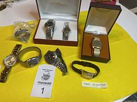 Overview of all watches arranged on yellow cloth including boxed pairs, individual watches, and band sealed in plastic.