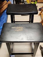 Top view photo showing wear and scratches on the black painted wooden seats of two barstools.