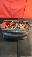 Photo showing black leather bag filled with mixed old keys with zipper open.