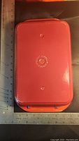 Top view of red Le Creuset rectangular cast iron pan lid showing embossed logo and lettering.