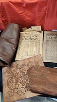 Photo showing clay template roll, two vintage leathercraft pattern booklets with floral designs, and carved leather pieces.