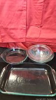 Set of five clear Pyrex glass items including three nested mixing bowls, one pie plate, and one rectangular baking dish.