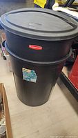 Rubbermaid black 32 gallon trash can with original fitted lid in place, showing brand logo and label on body.