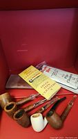 Various vintage pipes shown with pipe cleaners and leather bag inside display box