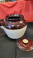 Stoneware crock bean pot with lid removed, showing interior and one handle, brown upper glaze and tan lower portion.