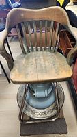 Front view of vintage barber chair showing wooden backrest and seat with signs of wear and crack in the wood.