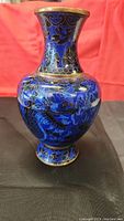 Front angle view of the blue brass vase with dragon design showing bulbous body and narrow neck with wide rim.
