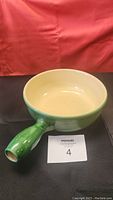 Side view of green ceramic fondue pot with handle showing cream-colored interior and overall good condition.