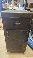 Closed view of vintage metal toolbox showing front cabinet door and top drawer with metal handles and black finish with rust