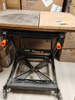 Front view of Black & Decker Workmate 350 portable workbench showing wooden top with dirt and wear, black metal frame with orange knobs, and wheels.