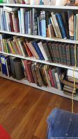 Three shelves filled with a variety of hardcover and paperback books of various colors and sizes arranged vertically and horizontally, mostly antique and classic literature and reference books.
