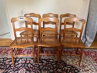 Photo showing all six chairs with solid wood frames and cane seats; four chairs have damaged cane seats.