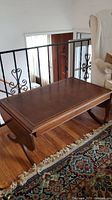 Rectangular coffee table with brown leatherette inlaid top and wooden legs, placed on wooden floor and rug.