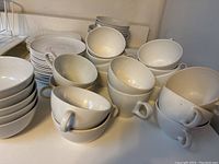 White coffee cups and saucers stacked with Snowhite Regency by Johnson Brothers plates in the background.