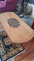 Top view of the oblong Hitchcock coffee table showing floral motif center and leaf border design, wood finish, and visible wear including a water ring.