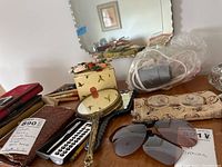 Worn leather wallets, handheld decorative fans, a metal pen, calculator, eyeglasses in case, and sunglasses shown on a wooden surface.
