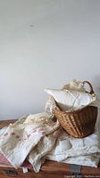Lot contents including folded linens with crochet and embroidery details, and a woven basket placed on top.