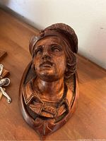 Close-up of wooden carved bust sculpture depicting a person wearing a hat with detailed facial features