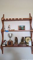Full view of three-tier wooden wall shelf displaying various trophies, figurines, and bookends