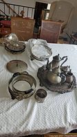 Full view of lot on table showing tea set, trays, butter dish, bowls, basket, and chafing dish holders.