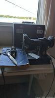 Overview showing machine beside closed case on table by window, includes scissors and book