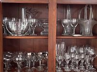 Two wooden shelves filled with various glassware and dishes including champagne coupes, cordial glasses, cut glass bowls and a basket with handle.