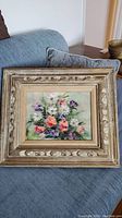 Full view of the framed floral still life oil painting resting on a blue couch