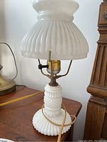 Full view of one vintage white milk glass table lamp on wooden surface, showing white milky glass shade and hobnail/ribbed textured base.