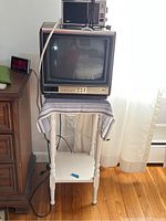 Side view of the Zenith 13 inch TV sitting on a small white wooden table with blue striped cloth cover, GE transistor radio and GE AM/FM radio on top of TV.
