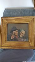 Full view of framed painting showing elderly couple in profile with gold-toned frame on grey couch.