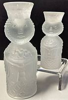 Two frosted glass wise men candleholders of different sizes displayed together against a black background, highlighting the textured and artistic embossing on the glass.