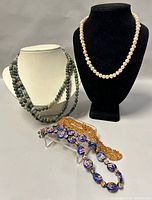 Group shot showing all four necklaces displayed on black and white stands